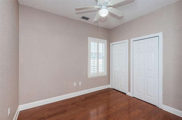 unfurnished bedroom with dark wood-style floors, visible vents, two closets, and baseboards