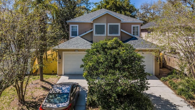 traditional-style home with fence, roof with shingles, an attached garage, stucco siding, and concrete driveway