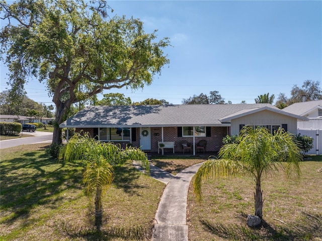 ranch-style home with a front lawn, a porch, fence, and brick siding