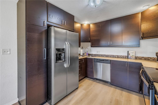 kitchen with light wood-style flooring, a sink, a textured ceiling, dark brown cabinetry, and appliances with stainless steel finishes