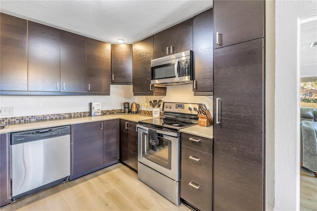 kitchen with light wood-style flooring, a textured ceiling, stainless steel appliances, dark brown cabinetry, and light countertops