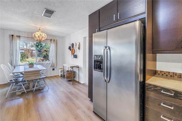 kitchen with visible vents, light wood finished floors, dark brown cabinets, stainless steel refrigerator with ice dispenser, and a textured ceiling