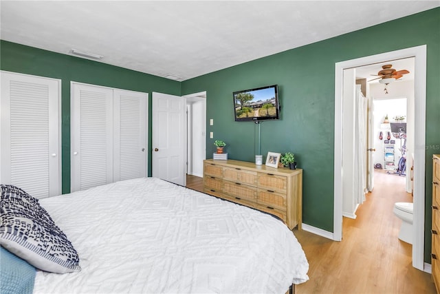 bedroom featuring visible vents, two closets, baseboards, and wood finished floors