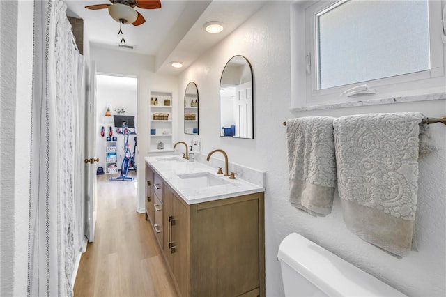 bathroom with ceiling fan, double vanity, wood finished floors, and a sink