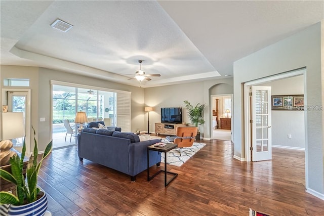 living room featuring a tray ceiling, wood finished floors, visible vents, and baseboards