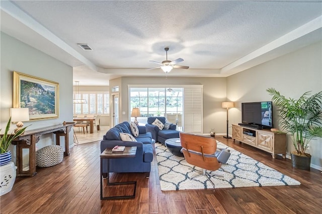 living room with visible vents, a textured ceiling, wood finished floors, baseboards, and ceiling fan