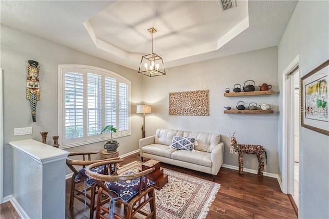 living room with visible vents, a raised ceiling, baseboards, and wood finished floors