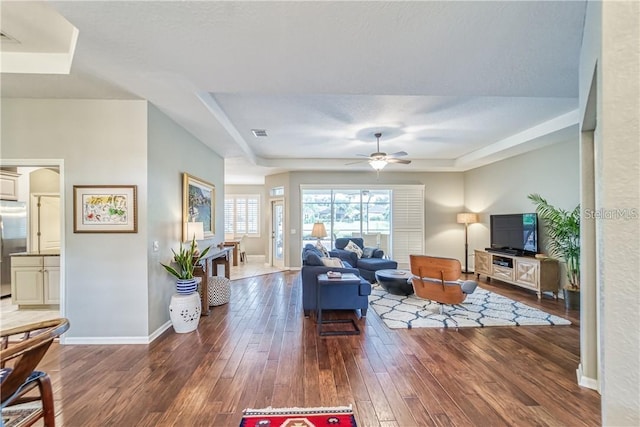 living room featuring visible vents, a raised ceiling, hardwood / wood-style floors, baseboards, and ceiling fan