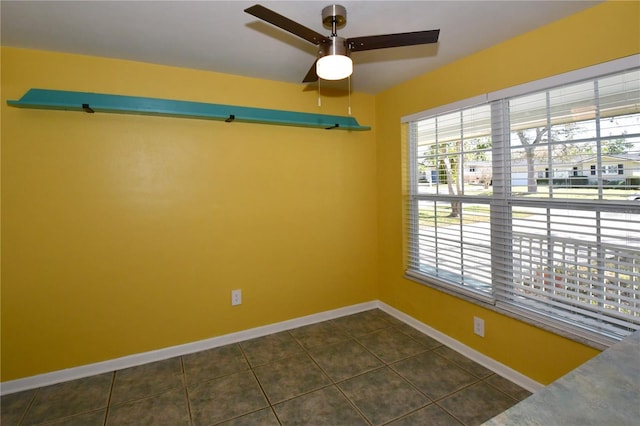 empty room with baseboards, a ceiling fan, and dark tile patterned flooring