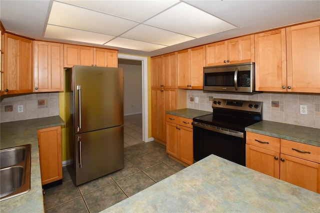 kitchen featuring backsplash, dark tile patterned flooring, appliances with stainless steel finishes, and a sink