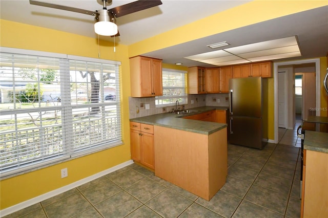 kitchen featuring baseboards, a peninsula, freestanding refrigerator, a sink, and backsplash