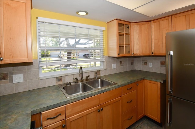 kitchen featuring dark countertops, glass insert cabinets, decorative backsplash, high end fridge, and a sink