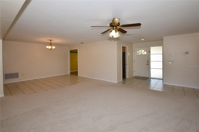 unfurnished living room featuring visible vents, ceiling fan with notable chandelier, light tile patterned floors, baseboards, and light colored carpet