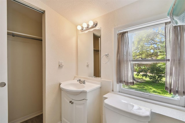 bathroom with a textured ceiling, toilet, vanity, and a textured wall