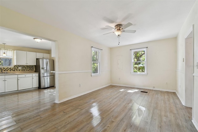 interior space with visible vents, light wood-style flooring, a ceiling fan, a sink, and baseboards