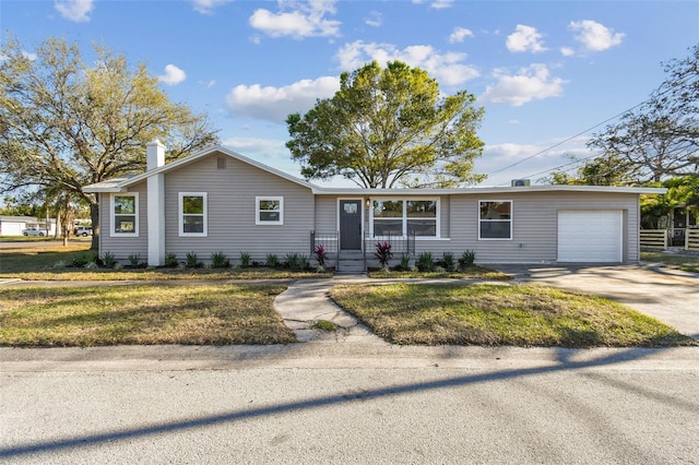 ranch-style house with a chimney, an attached garage, concrete driveway, and a front lawn