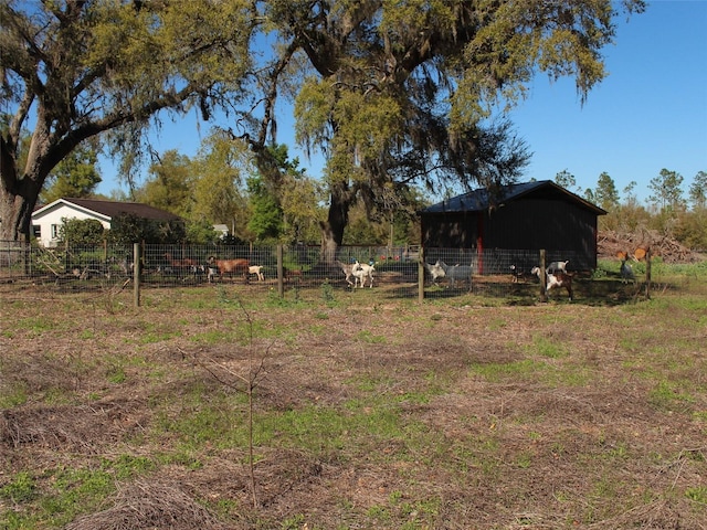 view of yard featuring a rural view, a pole building, an outdoor structure, and fence