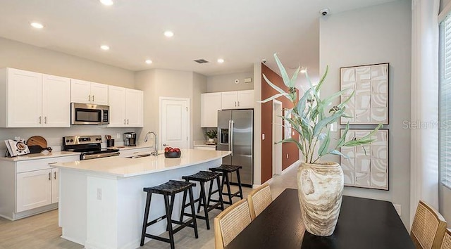 kitchen with appliances with stainless steel finishes, white cabinetry, a kitchen bar, and a sink