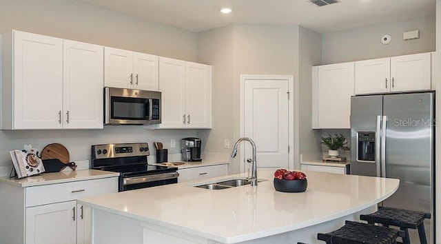 kitchen featuring a sink, a kitchen bar, appliances with stainless steel finishes, and white cabinets