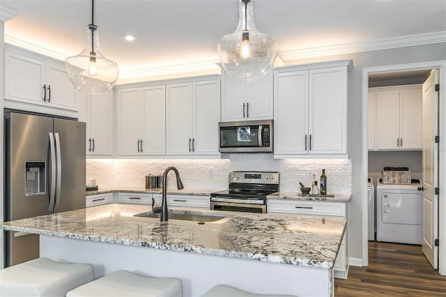 kitchen featuring washing machine and clothes dryer, a kitchen bar, ornamental molding, stainless steel appliances, and a sink