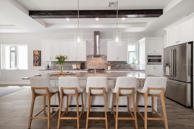 kitchen with beam ceiling, wall chimney range hood, tasteful backsplash, and appliances with stainless steel finishes