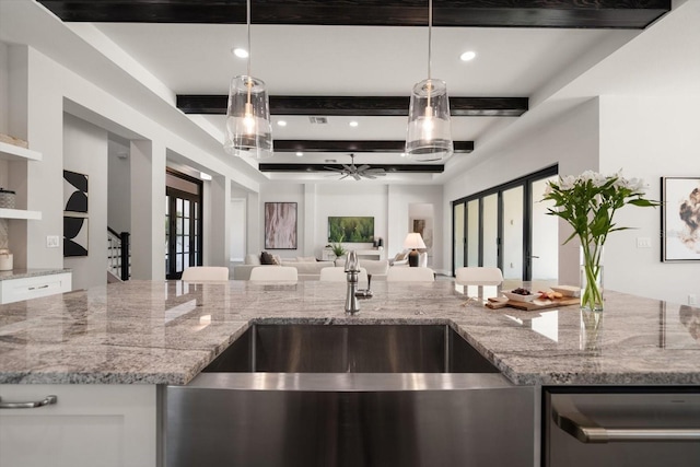 kitchen with beamed ceiling, a sink, open floor plan, white cabinets, and light stone countertops