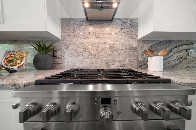 room details with decorative backsplash, light stone countertops, stainless steel range with gas cooktop, and white cabinets