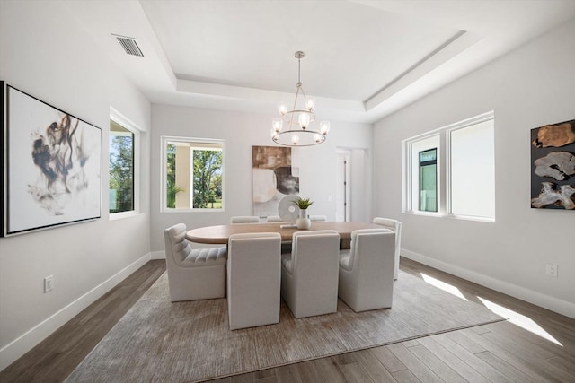 dining area featuring wood finished floors, visible vents, baseboards, a tray ceiling, and a notable chandelier