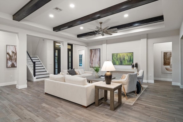 living area with stairway, baseboards, beam ceiling, ceiling fan, and light wood-type flooring