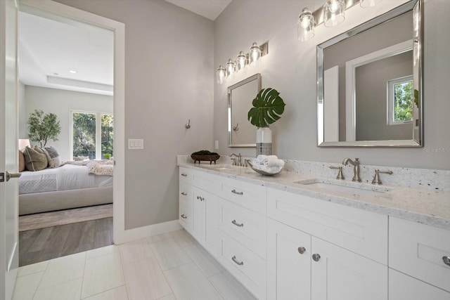 ensuite bathroom with a sink, baseboards, ensuite bath, and double vanity