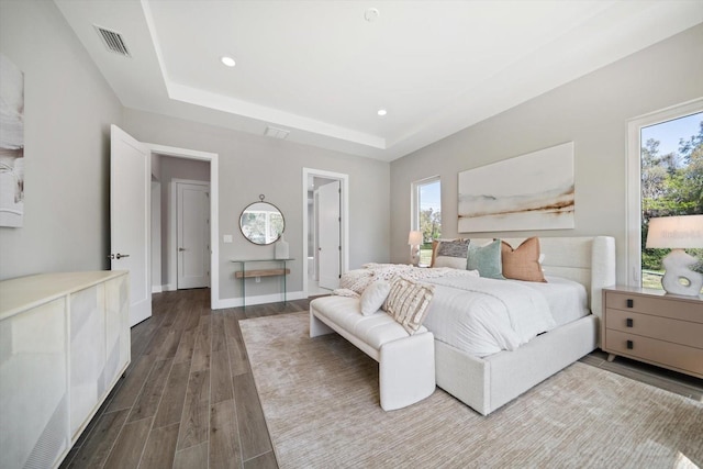 bedroom with visible vents, a raised ceiling, multiple windows, and wood finished floors