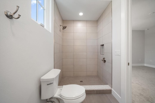 full bath featuring tiled shower, toilet, and baseboards