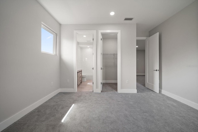 unfurnished bedroom with baseboards, visible vents, a spacious closet, ensuite bathroom, and light colored carpet