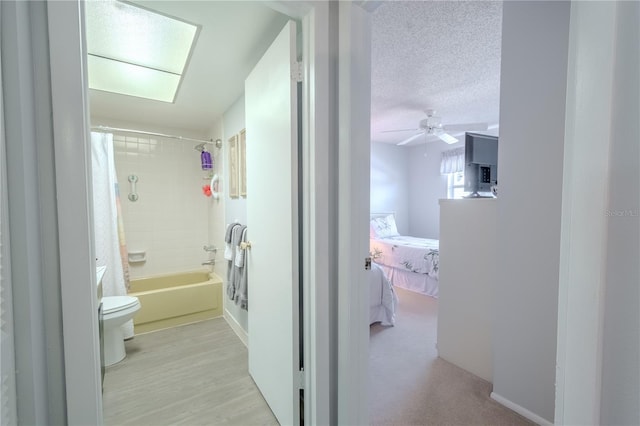 ensuite bathroom featuring toilet, ensuite bathroom, a textured ceiling, shower / bath combination with curtain, and ceiling fan