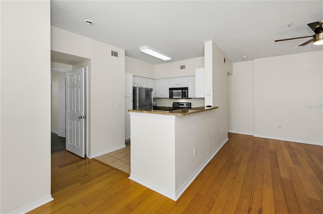 kitchen featuring white cabinets, visible vents, ceiling fan, stainless steel microwave, and freestanding refrigerator