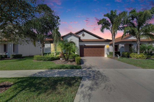 view of front of property with decorative driveway, an attached garage, a lawn, and stucco siding