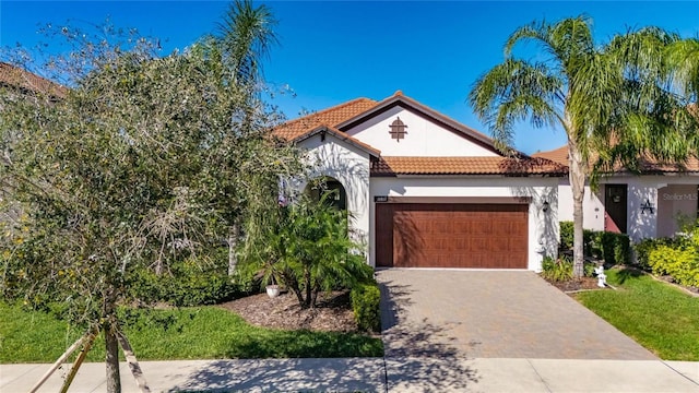 mediterranean / spanish-style home with stucco siding, a tiled roof, decorative driveway, and a garage