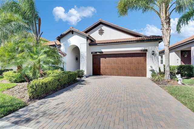 mediterranean / spanish-style home with stucco siding, a tile roof, decorative driveway, and a garage