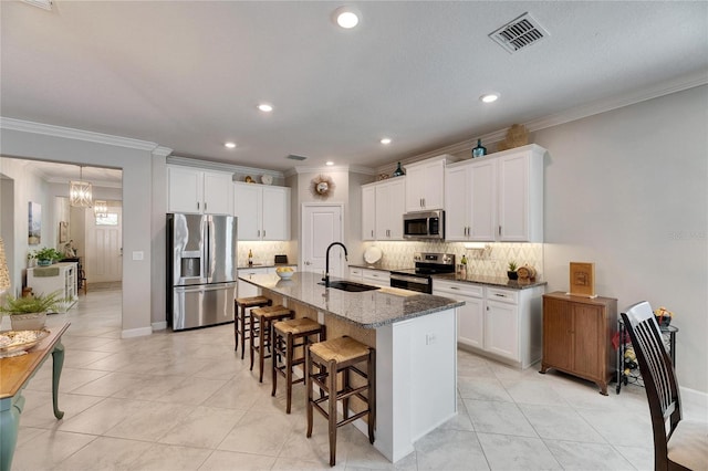 kitchen with visible vents, a breakfast bar, a kitchen island with sink, a sink, and stainless steel appliances