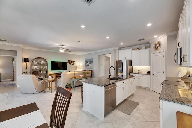 kitchen with open floor plan, a center island with sink, dark stone counters, stainless steel appliances, and a sink