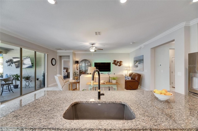 kitchen featuring visible vents, crown molding, open floor plan, light stone counters, and a sink