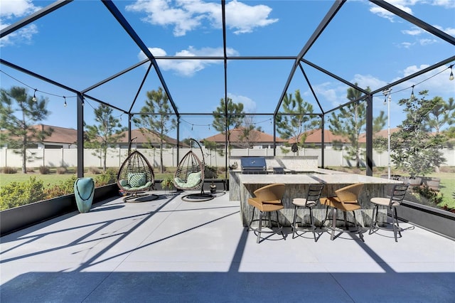 view of patio / terrace featuring glass enclosure, outdoor wet bar, fence, and an outdoor kitchen