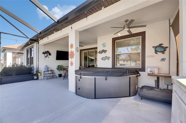 view of patio / terrace featuring glass enclosure, a hot tub, and a ceiling fan