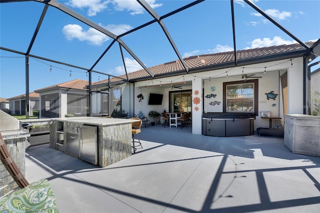 view of patio with an outdoor kitchen, a hot tub, glass enclosure, and a ceiling fan