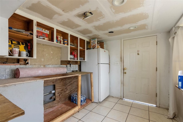 kitchen with light tile patterned floors, open shelves, light countertops, and freestanding refrigerator