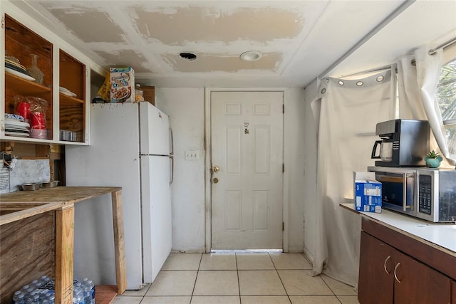 kitchen with stainless steel microwave, light tile patterned flooring, light countertops, and freestanding refrigerator