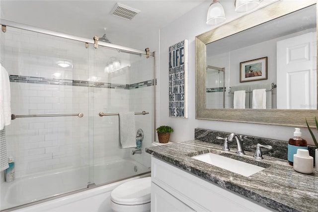 bathroom with visible vents, toilet, vanity, and bath / shower combo with glass door