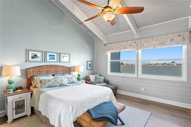 bedroom featuring a ceiling fan, lofted ceiling with beams, wood finished floors, wooden walls, and baseboards