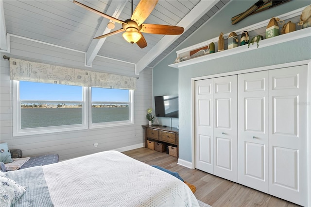 bedroom with light wood finished floors, baseboards, wood walls, lofted ceiling with beams, and a closet