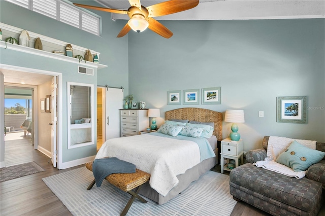 bedroom featuring visible vents, baseboards, a barn door, a high ceiling, and wood finished floors